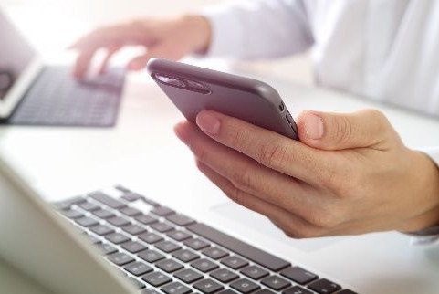 Hand holding cell phone over a laptop